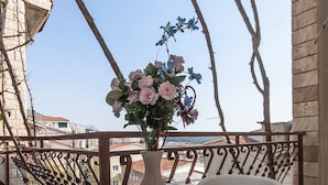 Un balcone con un tavolo rotondo e un vaso di fiori, una sedia bianca in plastica, e vista su edifici sullo sfondo.