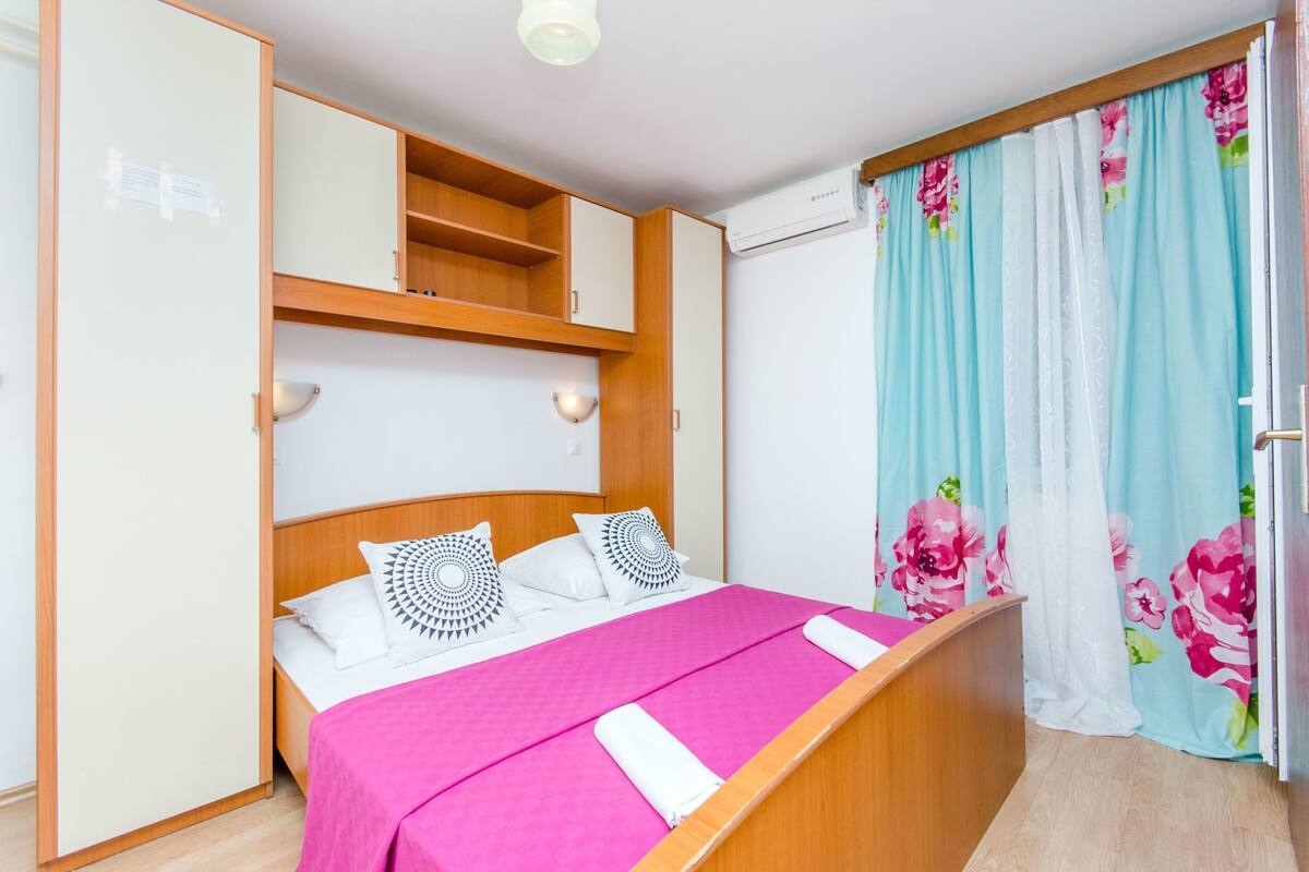 Ein Schlafzimmer mit einem Bett, einem Holzschrank und einem Fenster mit blumigen Vorhängen.