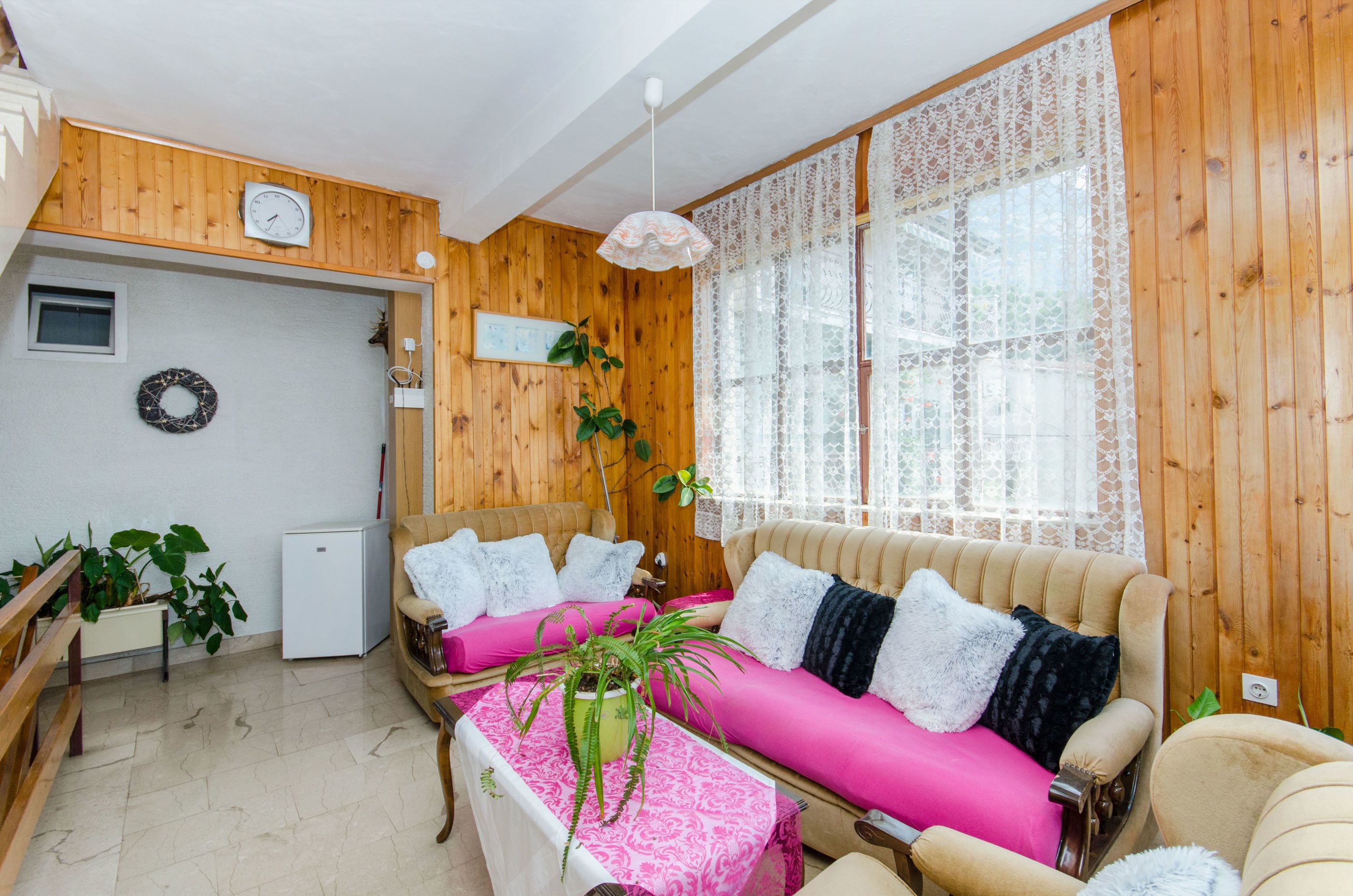 A cozy room with wooden walls, a sofa with pink cushions, a small table with a plant, and a white ceiling fan.