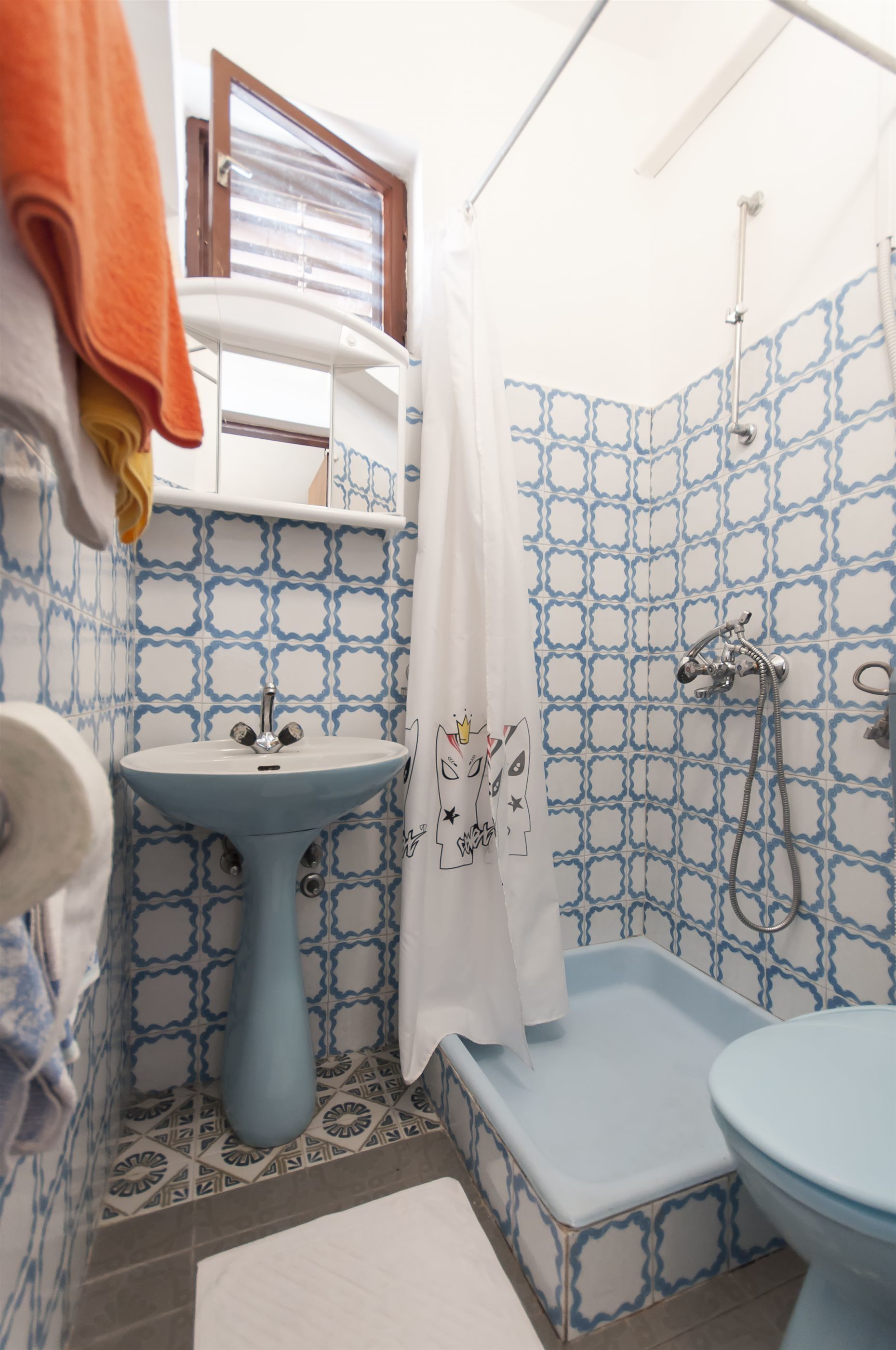 Een badkamer met een wastafel, toilet, douche en een raam.