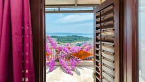Un balcone con vista su un paesaggio montuoso, una ringhiera rossa e fiori viola.
