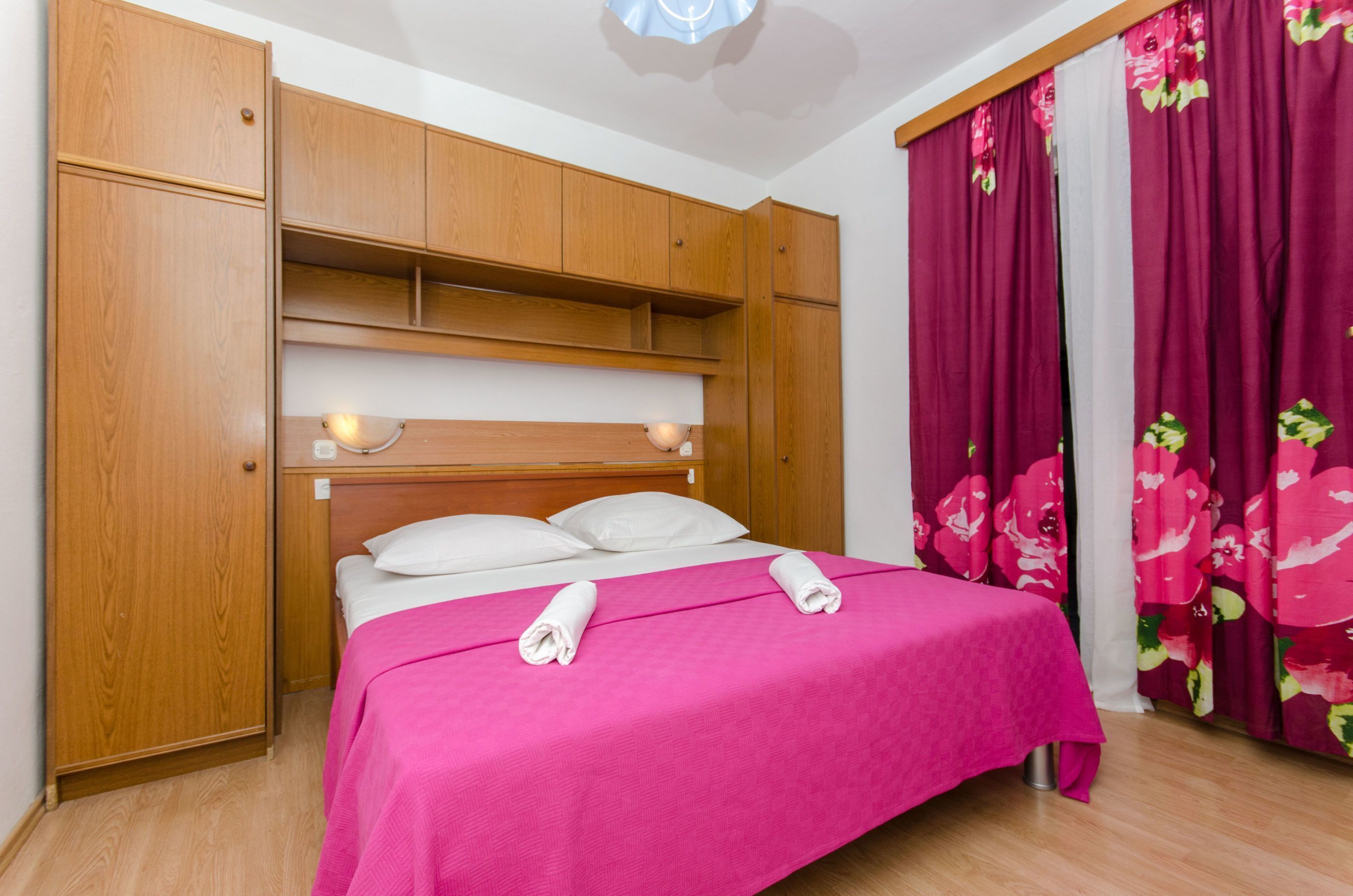 A bedroom with a bed, wooden wardrobe, and a window with curtains.