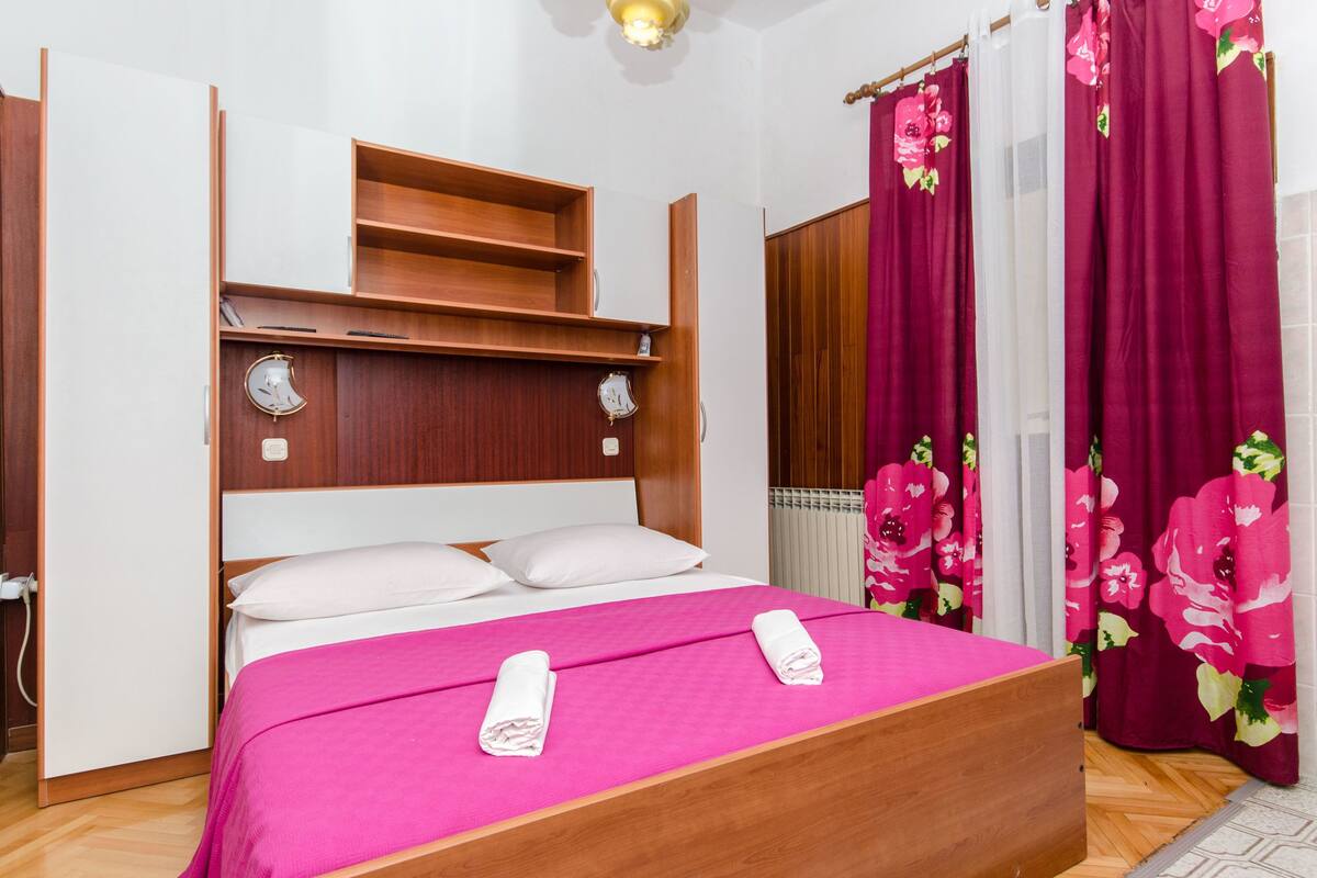 Ein Hotelzimmer mit einem hölzernen Bett, einem Regal darüber und einem Fenster mit roten Vorhängen.