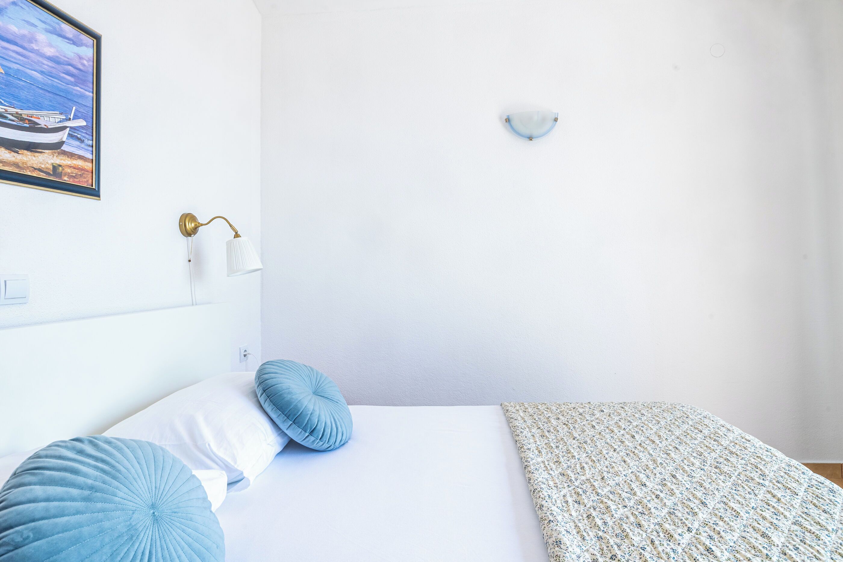 Une chambre bien rangée, avec un lit, des oreillers, une lampe fixée au mur, un tableau et un petit objet décoratif fixé au mur.