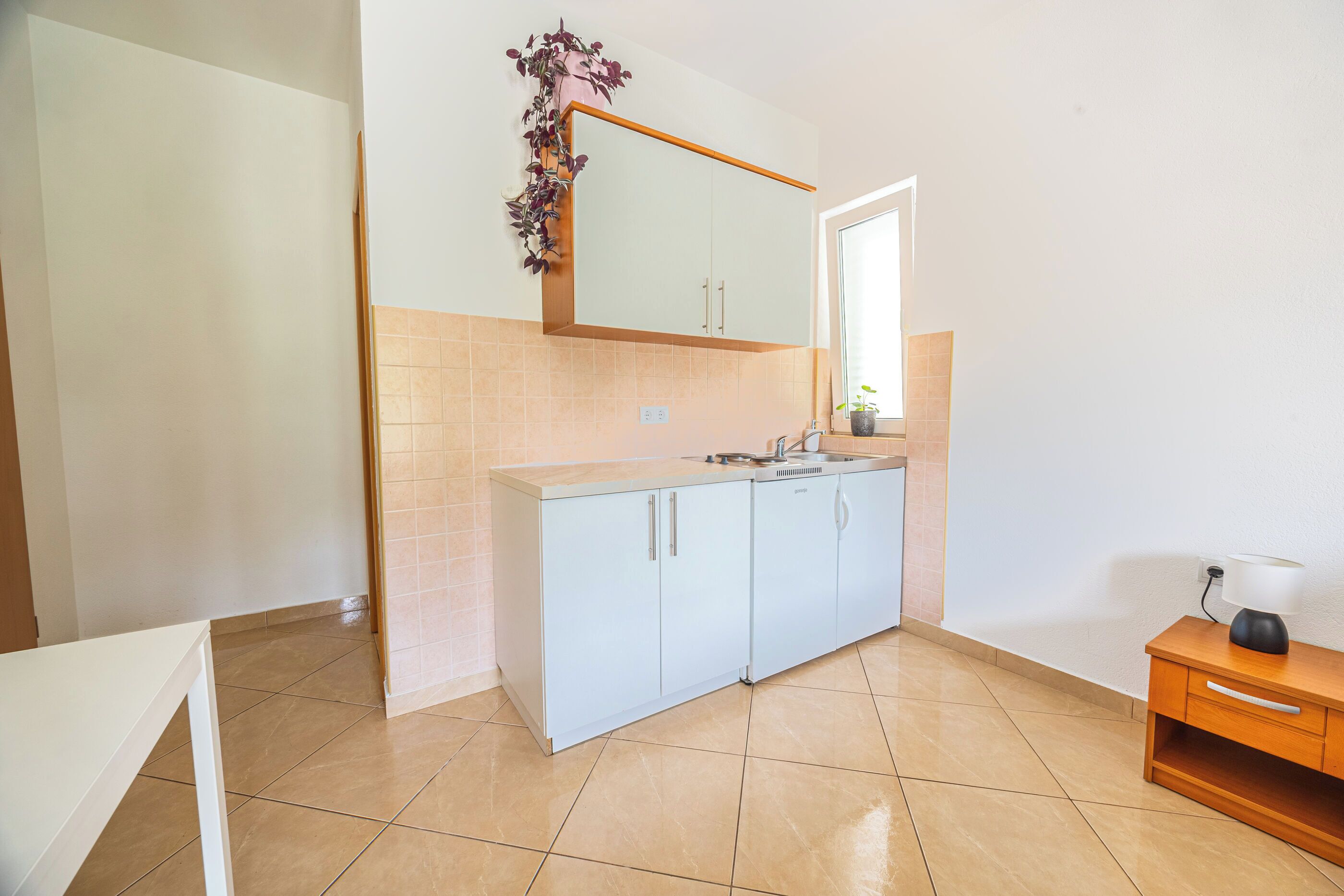 A kitchen with light blue cabinets, a white countertop, and a wooden cabinet with a lamp.