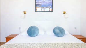 Una cama bien hecha con dos almohadas, un cuadro enmarcado de un barco en la playa y dos lámparas de pared.