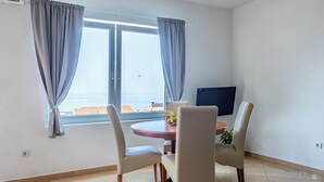 Un comedor con una mesa redonda, dos sillas, un frutero y un televisor en la pared.