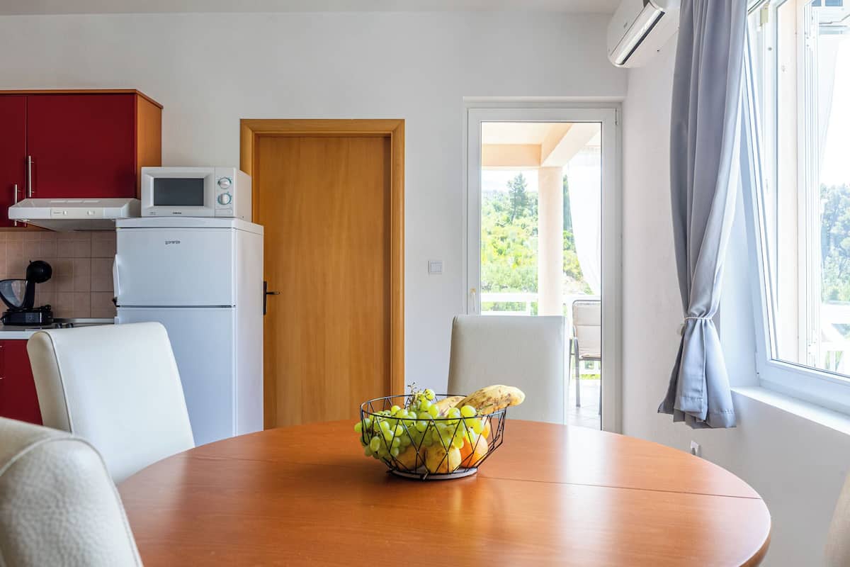 A kitchen with a microwave, a refrigerator, and a dining table with a fruit bowl.