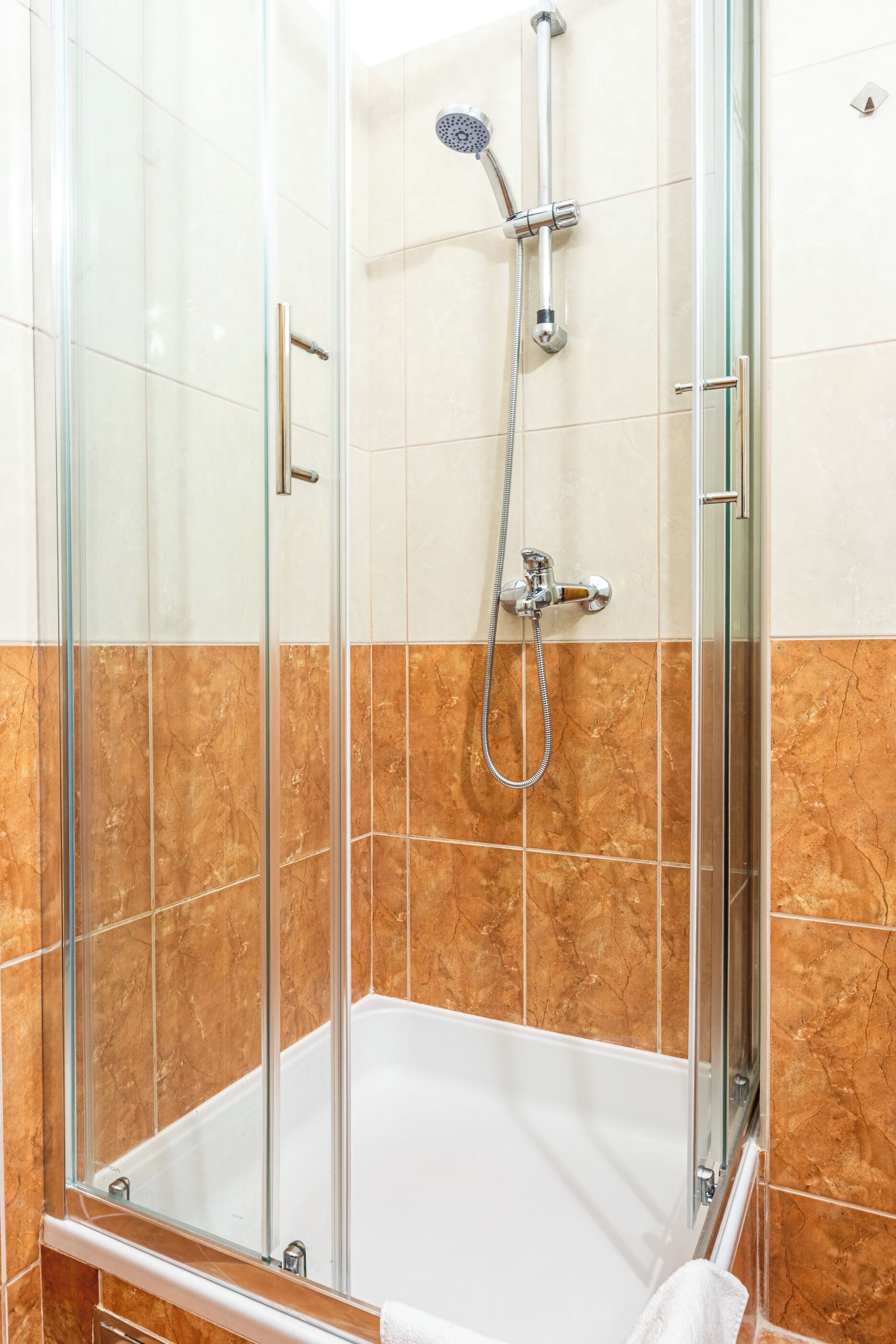 A glass-enclosed shower with a handheld showerhead and a wall-mounted faucet.