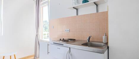 A compact kitchen with a built-in stove, sink, and a window with a curtain.