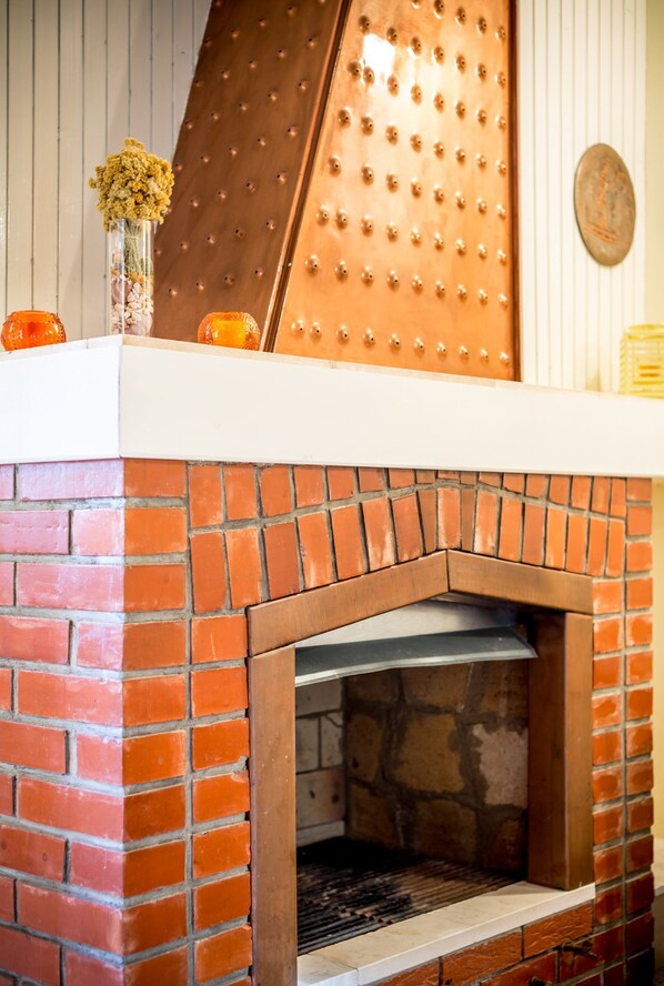 A brick fireplace with a metal door, a vase with dried flowers, and two orange candles on the mantel. - Apartment Srecko (Vinisce)