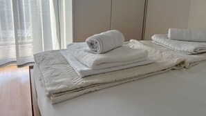 A neatly made bed with folded white towels and a textured blanket. - Apartments Marija Jug (Primosten)