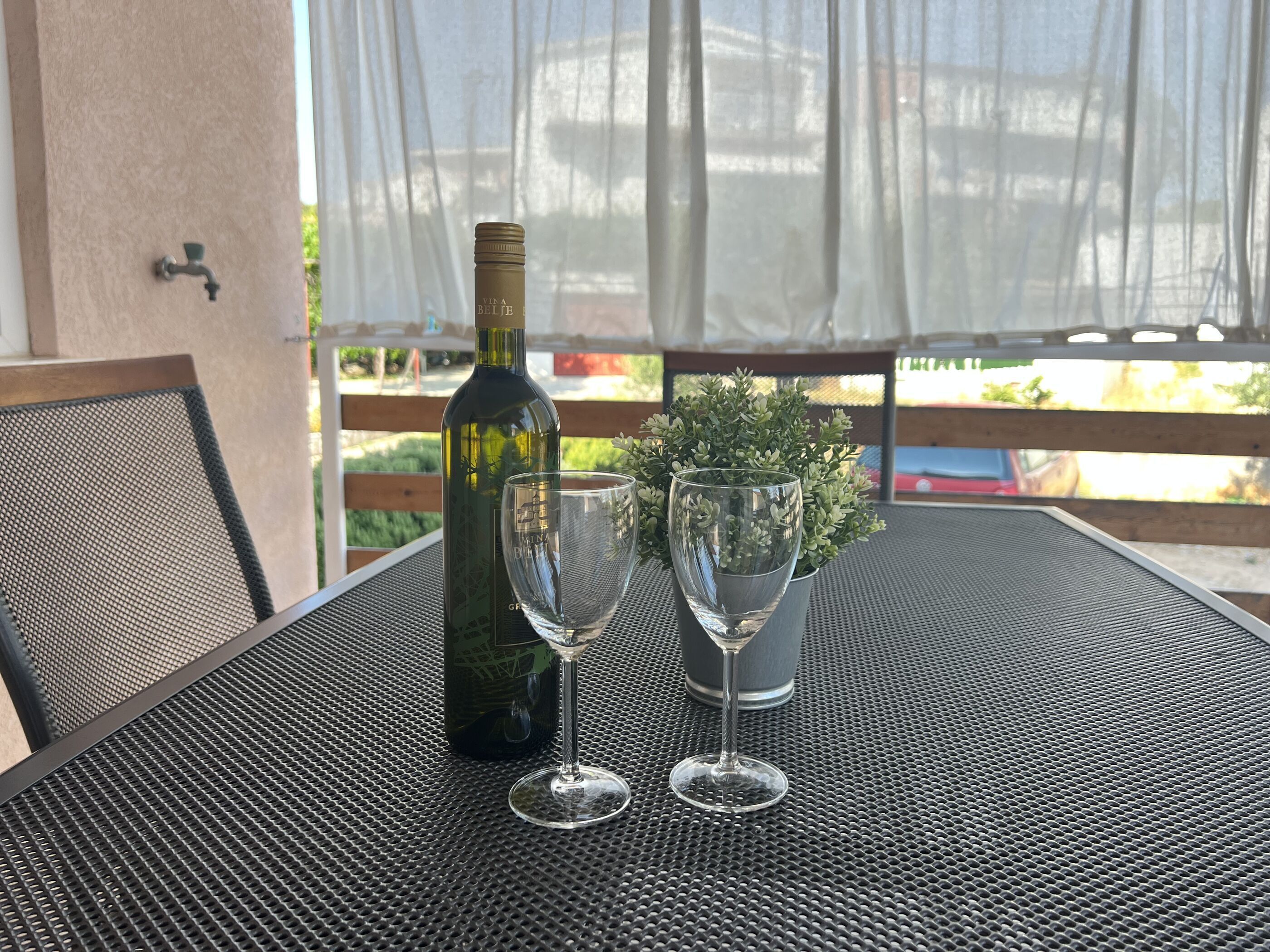 Une table avec une bouteille de vin et deux verres à vin, placée sur une table d’extérieur à surface texturée.