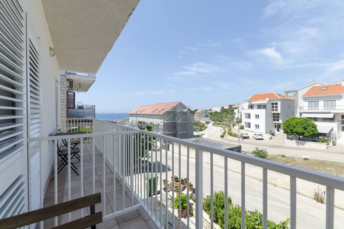 A balcony with a view of a residential street, a clear sky, and a distant body of water.