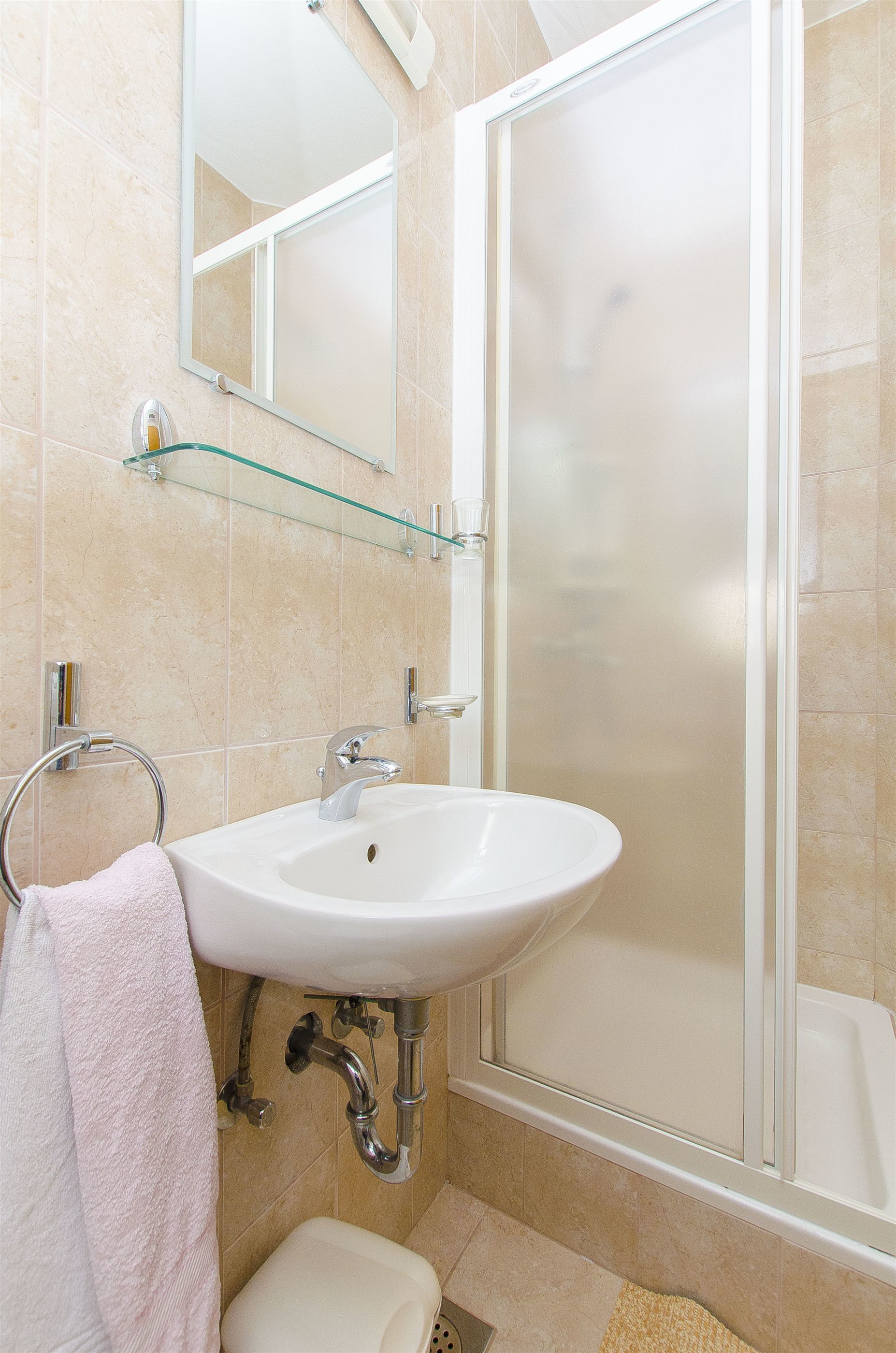 A bathroom with a white sink, a glass shelf, a mirror, and a shower enclosure.