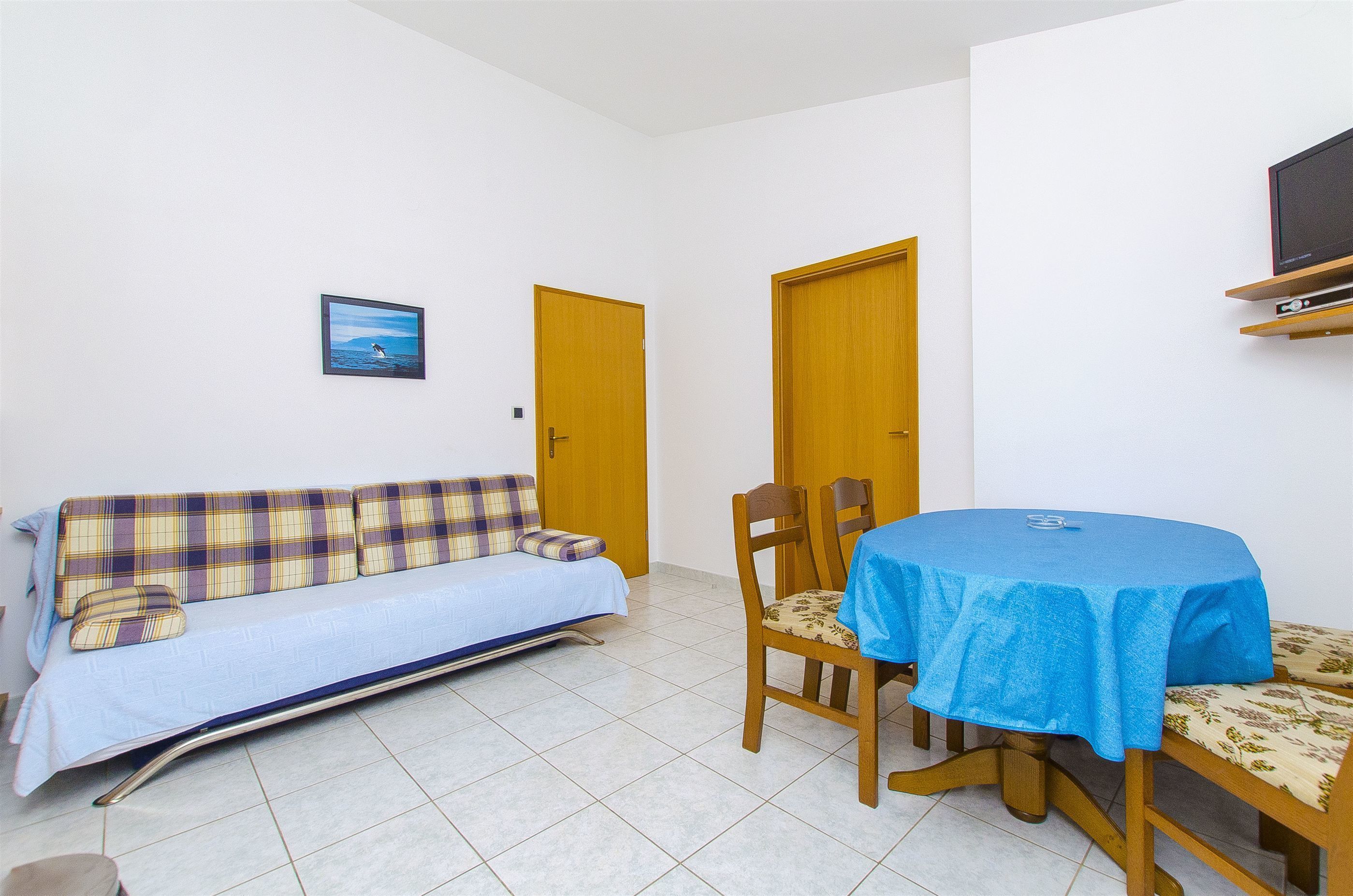 A room with a sofa, a dining table with a blue tablecloth, and two wooden doors.