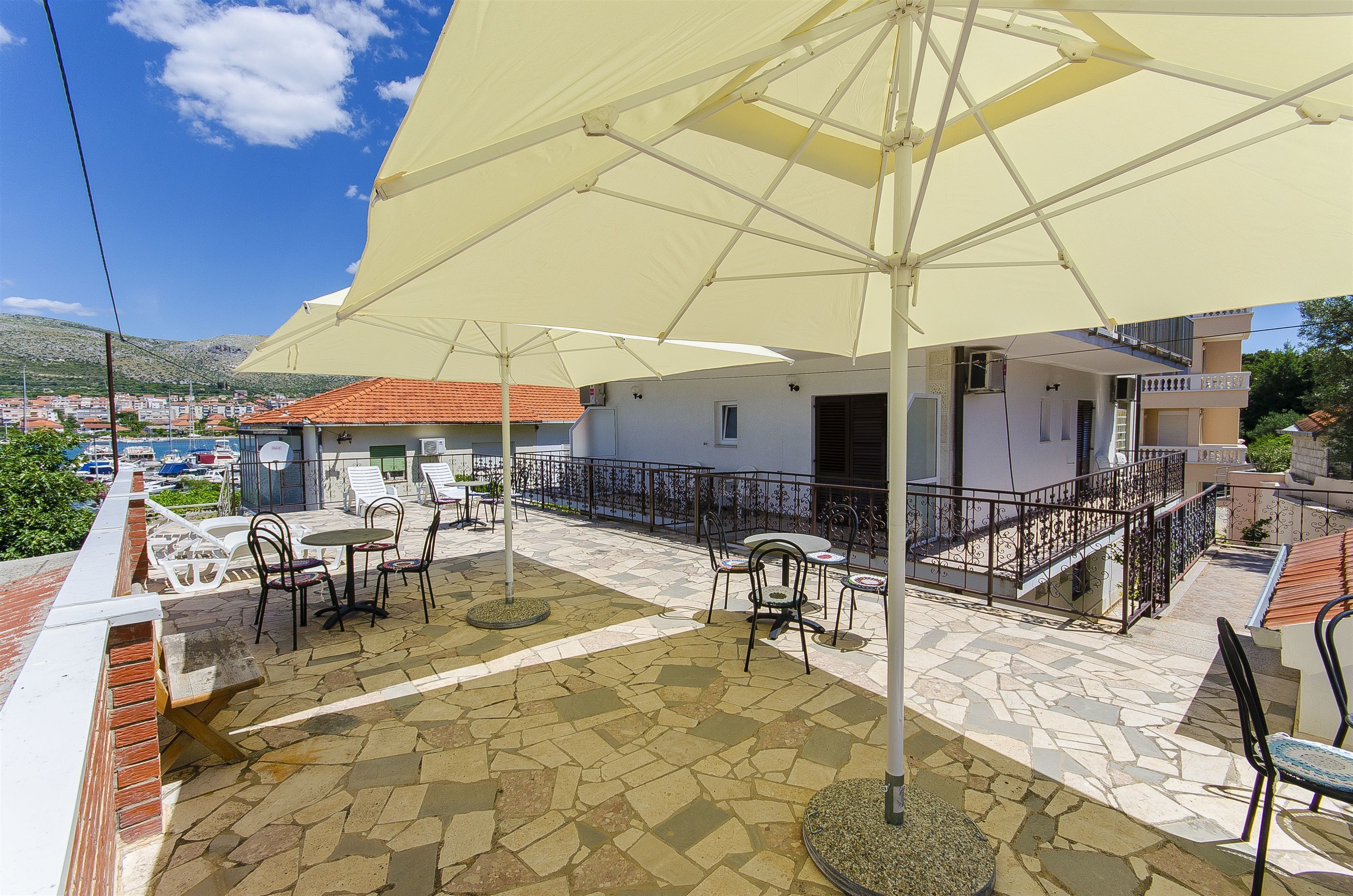 A terrace with outdoor seating, a large umbrella, and a view of the town and hills in the background.
