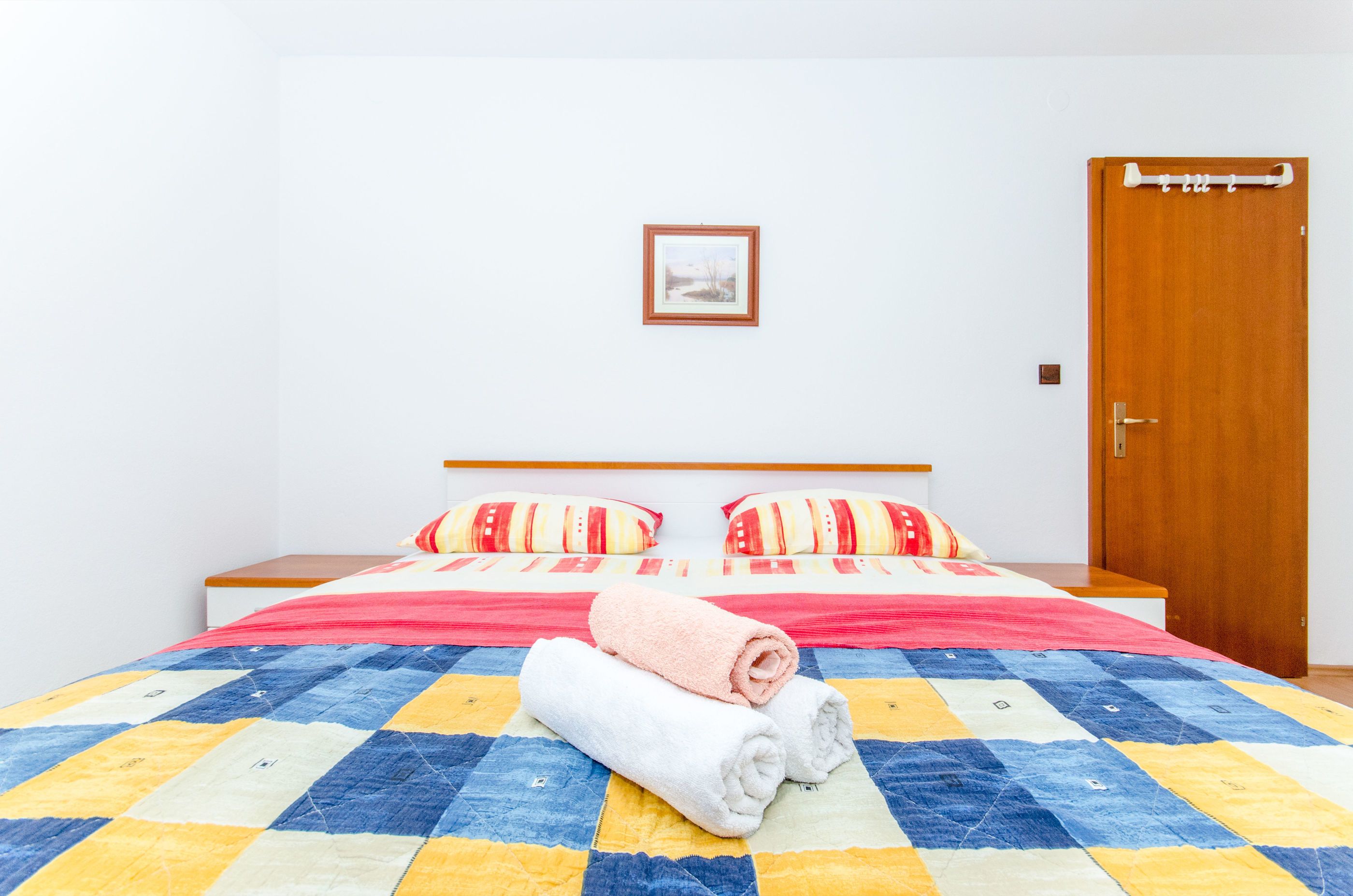 Un letto rifatto con cura, una coperta a quadri, due cuscini e due asciugamani arrotolati.