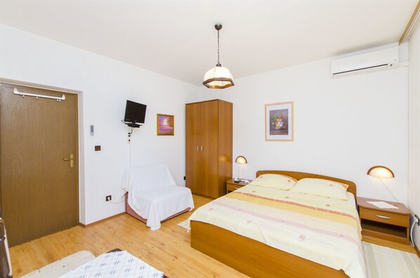 A bedroom with a wooden bed, bedside lamps, a wardrobe, a television, and an air conditioning unit. - Apartments and Rooms Iva (Trogir)