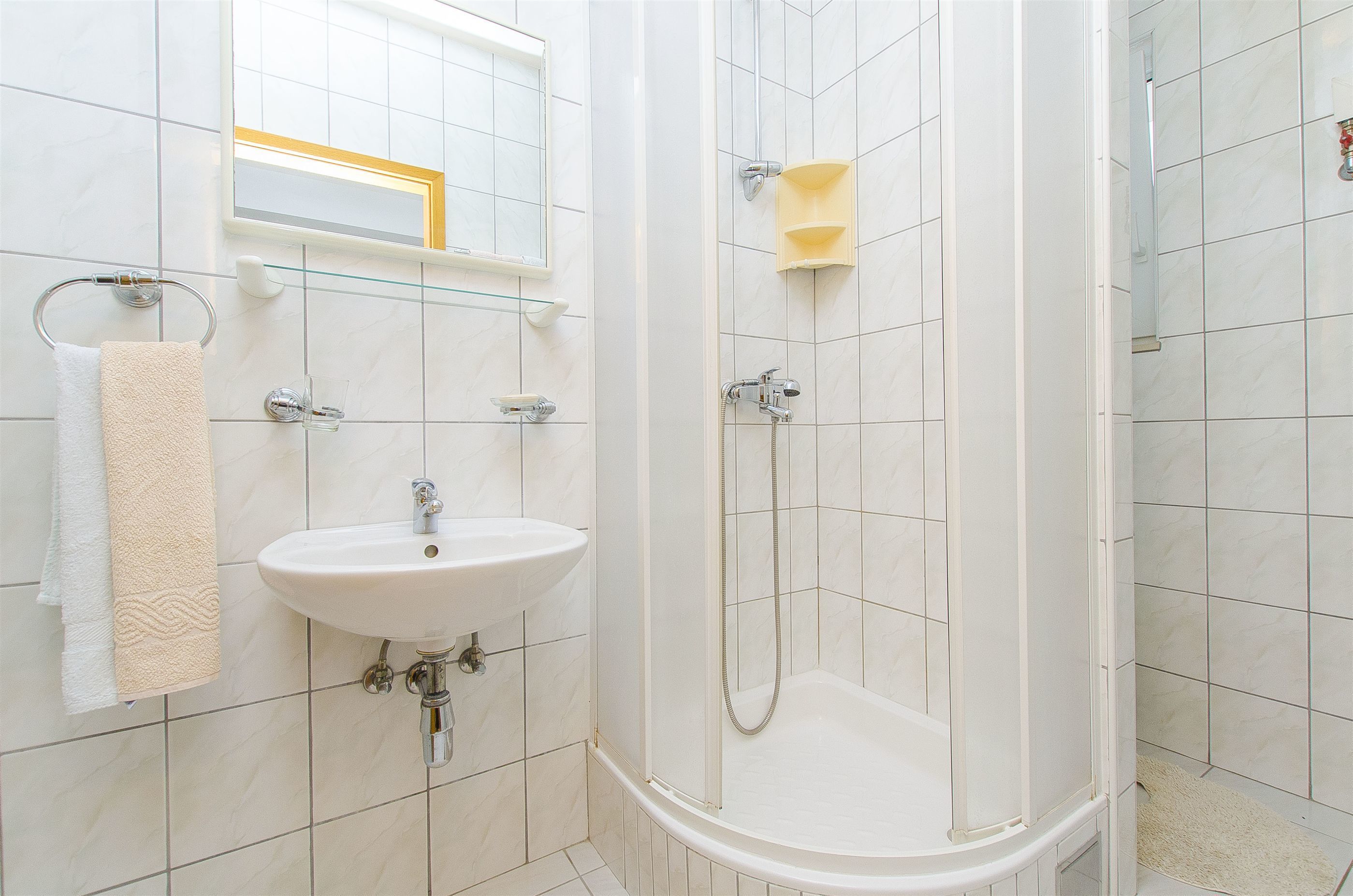 A bathroom with a white sink, a glass shelf, a towel rack, and a shower with a glass door.