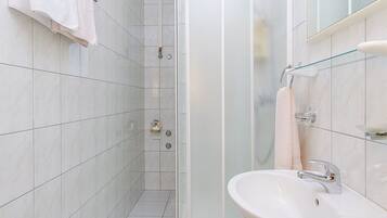 Un baño moderno con baldosas blancas, cabina de ducha de vidrio, lavamanos con espejo y toallero.