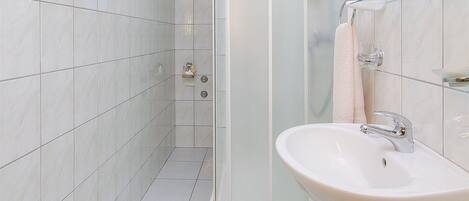 Un baño moderno con baldosas blancas, cabina de ducha de vidrio, lavamanos con espejo y toallero.