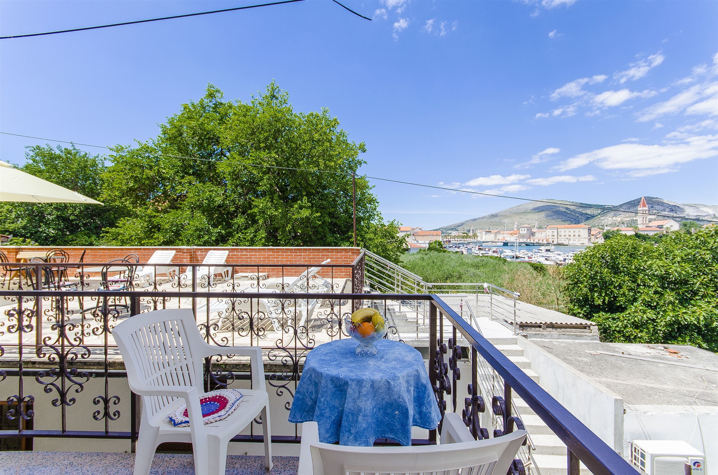 A balcony with a table and chairs, a railing, and a view of a cityscape with buildings and a mountain in the background.