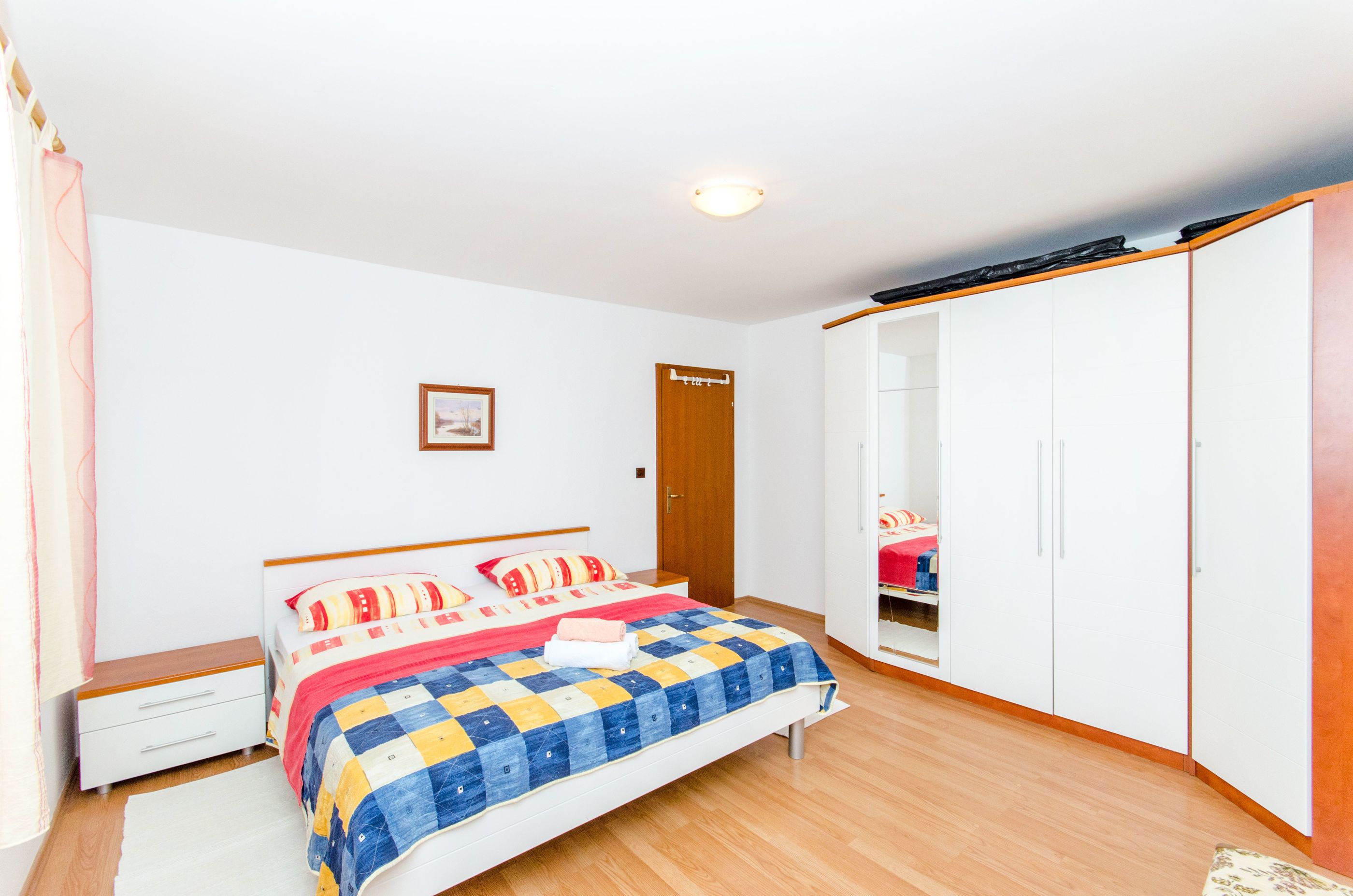 A bedroom with a bed, a wardrobe, a bedside table, and a door.