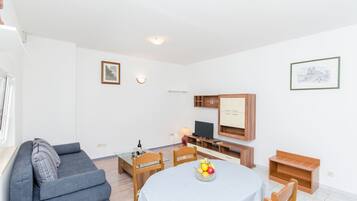Una sala de estar moderna con un sofá gris, una mesa de comedor con frutero, un televisor y armarios de madera.