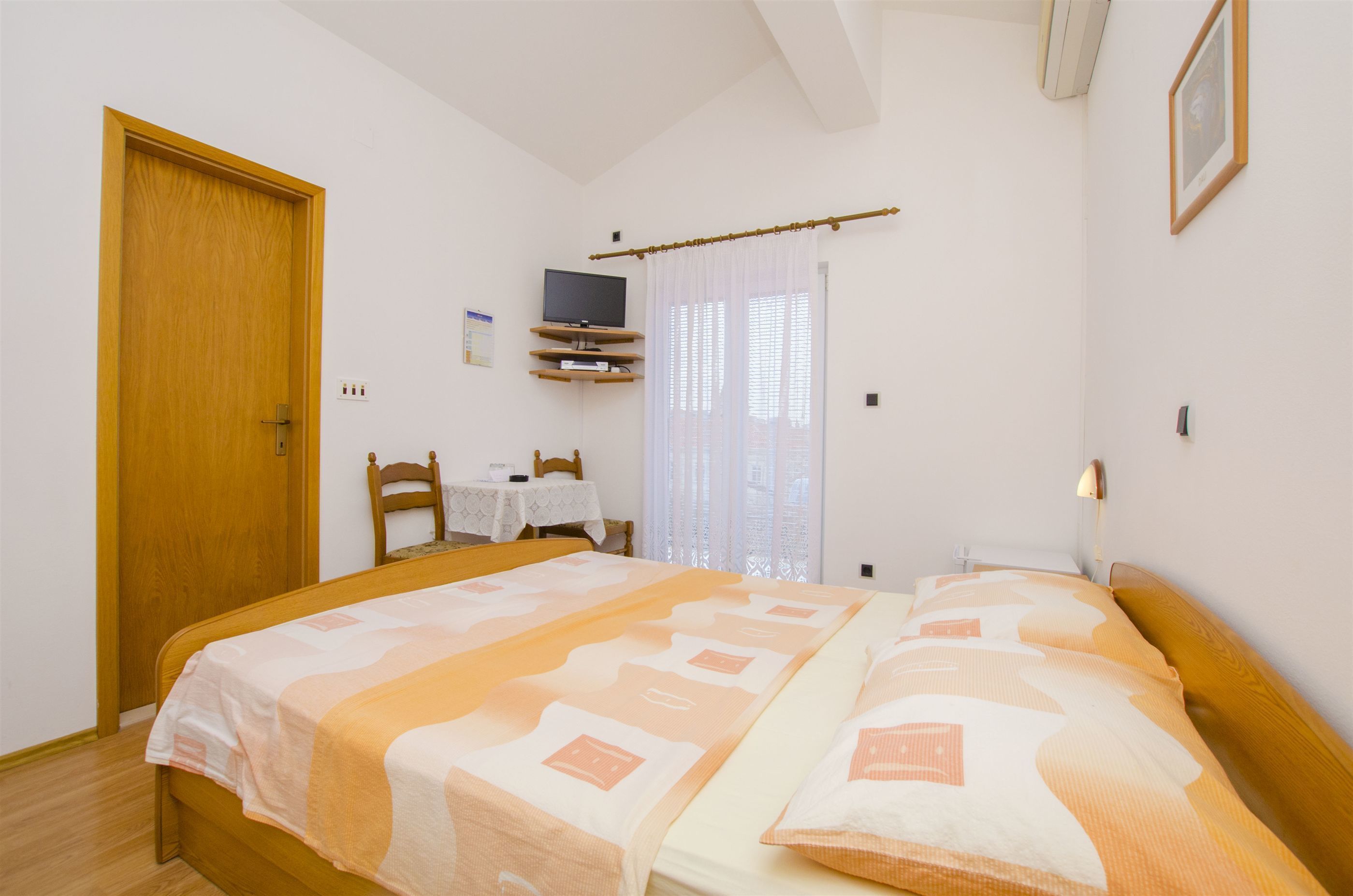 A bedroom with two beds, a TV on a stand, a table with a chair, and a window with curtains.