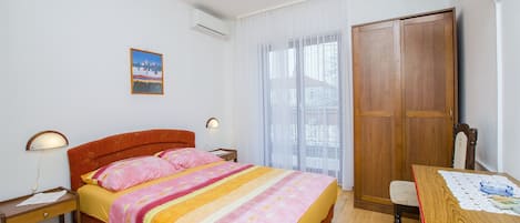 Une chambre à coucher comprenant un lit, des tables de chevet, une armoire en bois, un bureau avec une chaise et une fenêtre avec des rideaux.