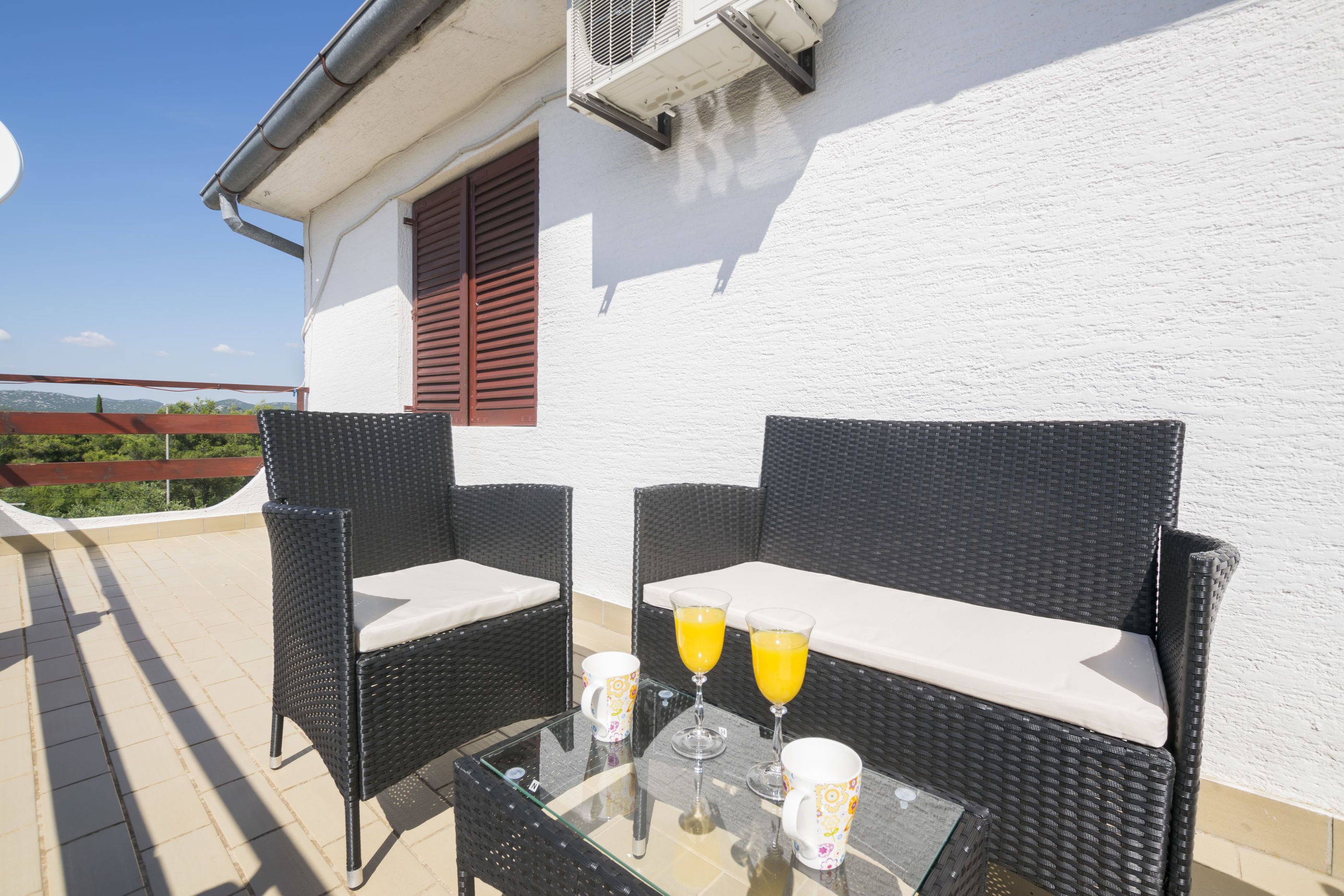 Une terrasse avec des meubles en osier, deux verres de jus d’orange et une table.