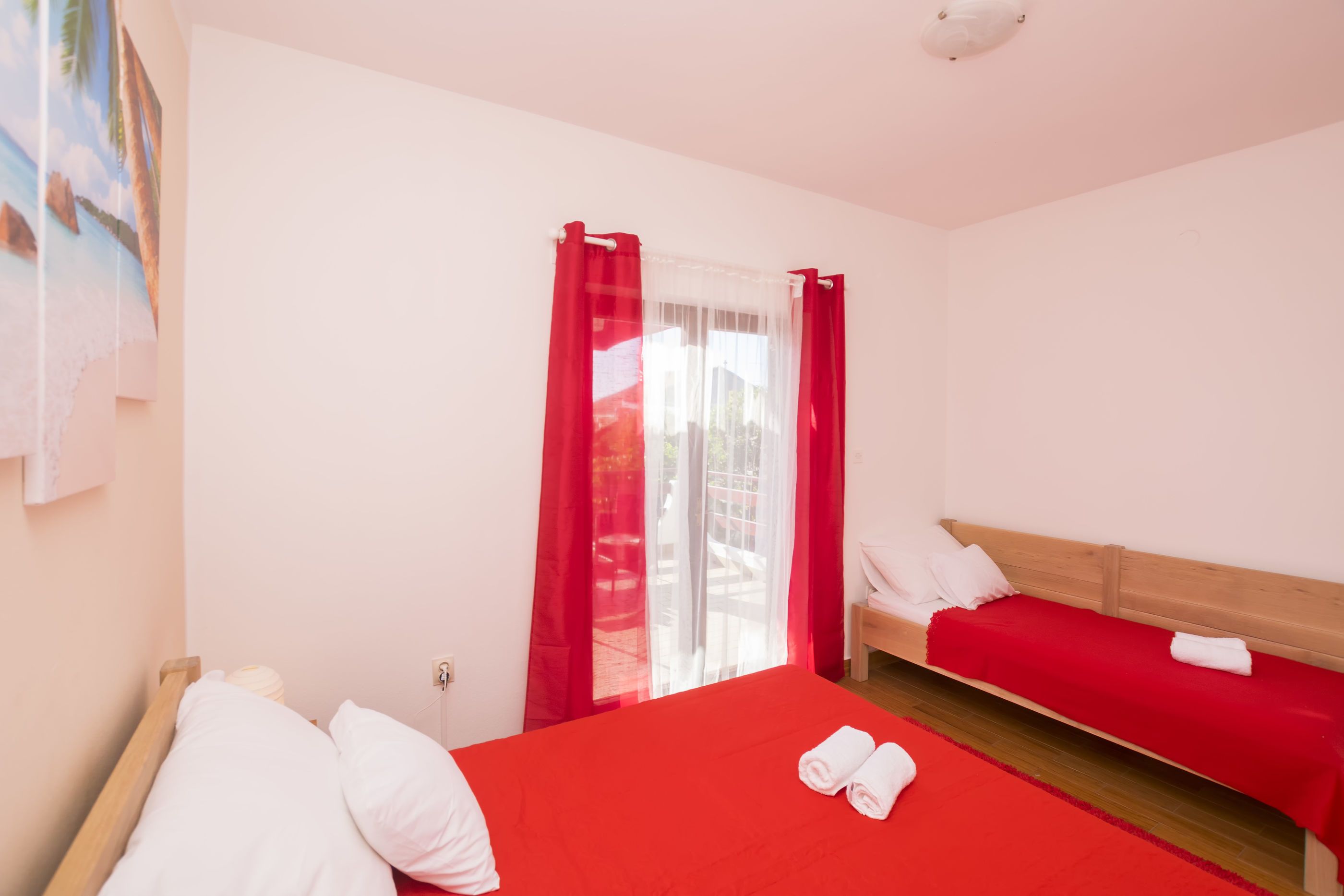 A hotel room with a red bedspread, white pillows, and a red curtain.