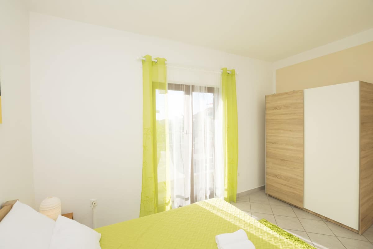 A bedroom with a bed, a wardrobe, and a window with sheer curtains.