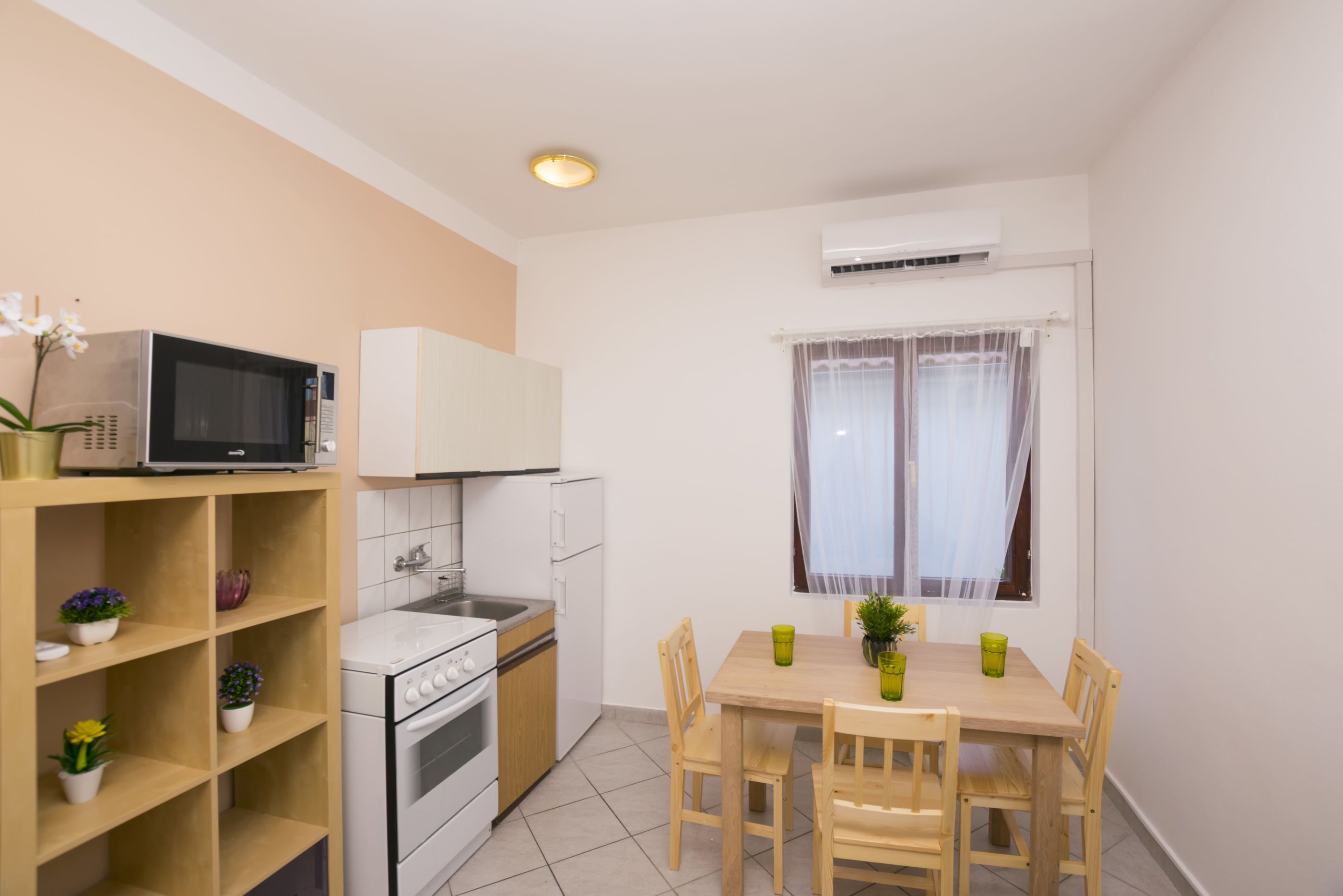 A compact kitchen with a microwave, stove, and sink. There is a dining table with chairs and a window with curtains.