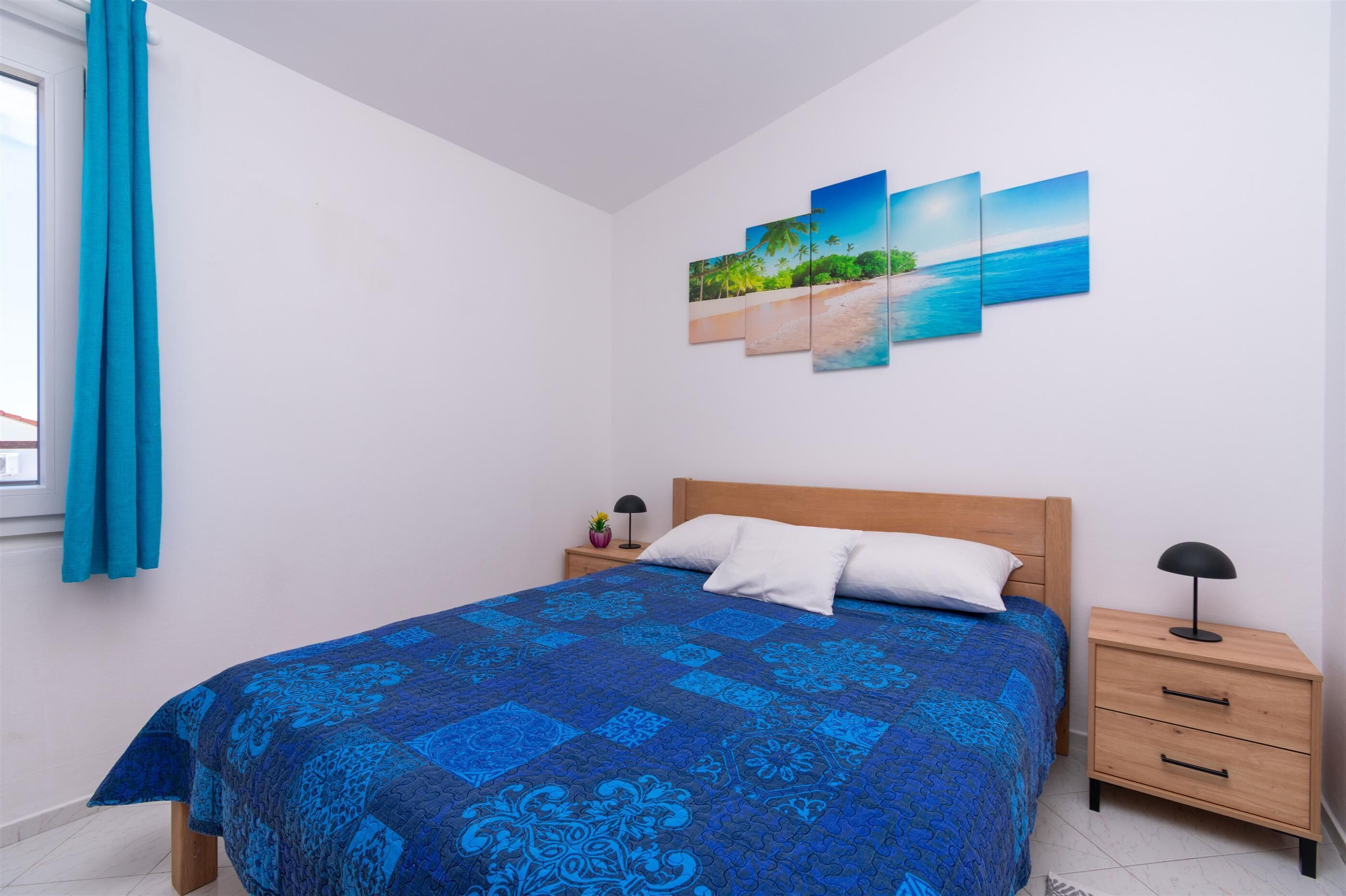 A bedroom with a bed, a nightstand, a wall-mounted artwork, and a window with curtains.