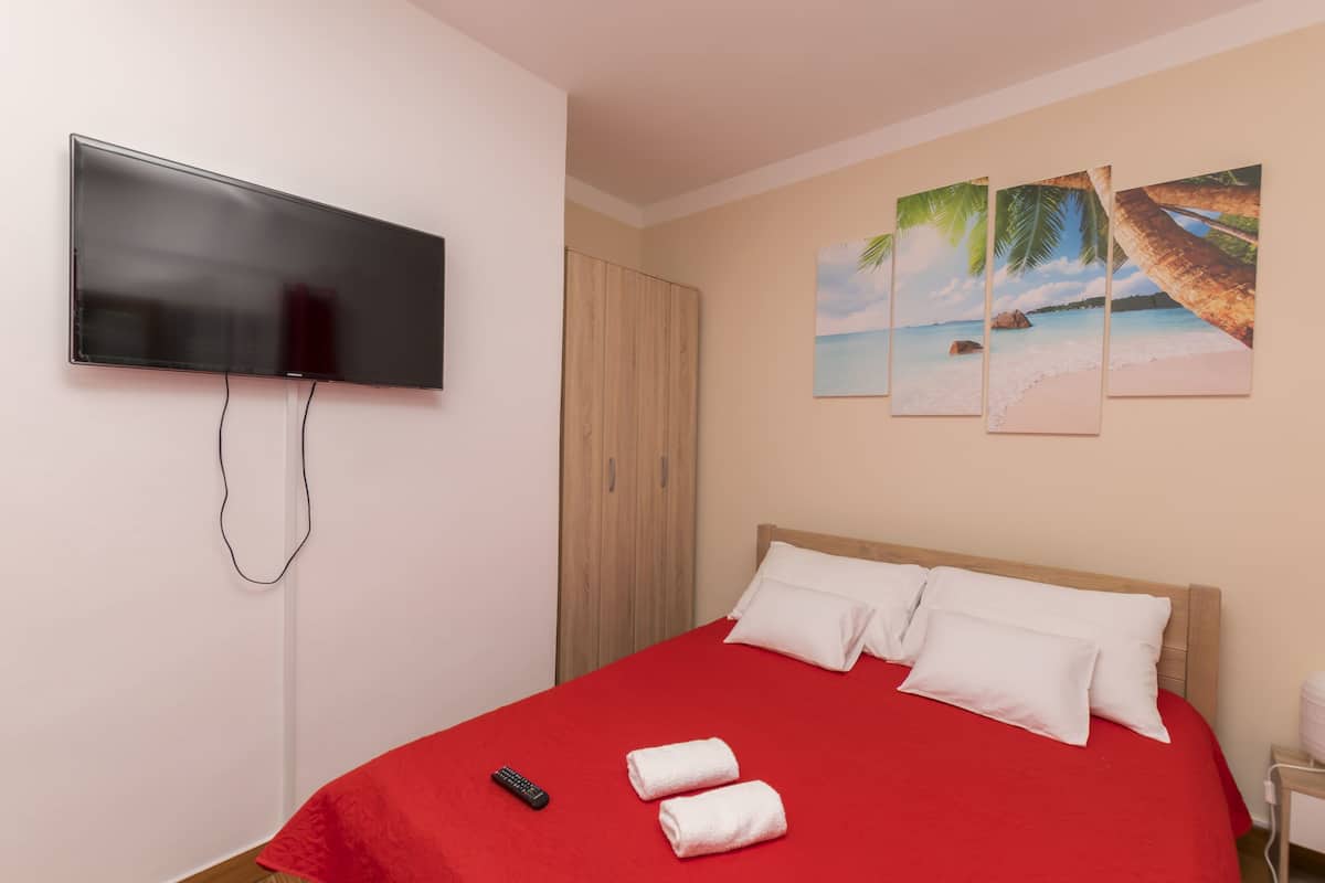 A hotel room with a bed, a TV mounted on the wall, and a beach-themed painting.