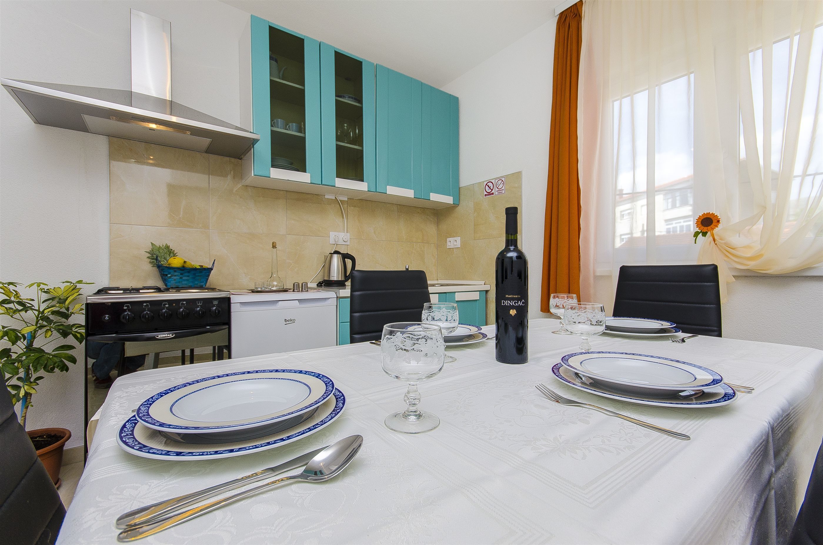 A dining area with a table set for four, a bottle of wine, and a view of the kitchen in the background.