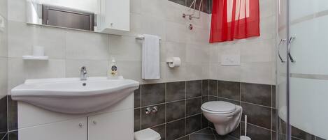 Un baño con lavamanos, inodoro y ducha blancos. Hay una cortina roja y una toalla blanca colgada en la pared.
