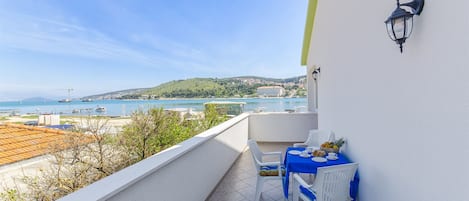 A balcony with a table and chairs, overlooking a coastal view with buildings and greenery.