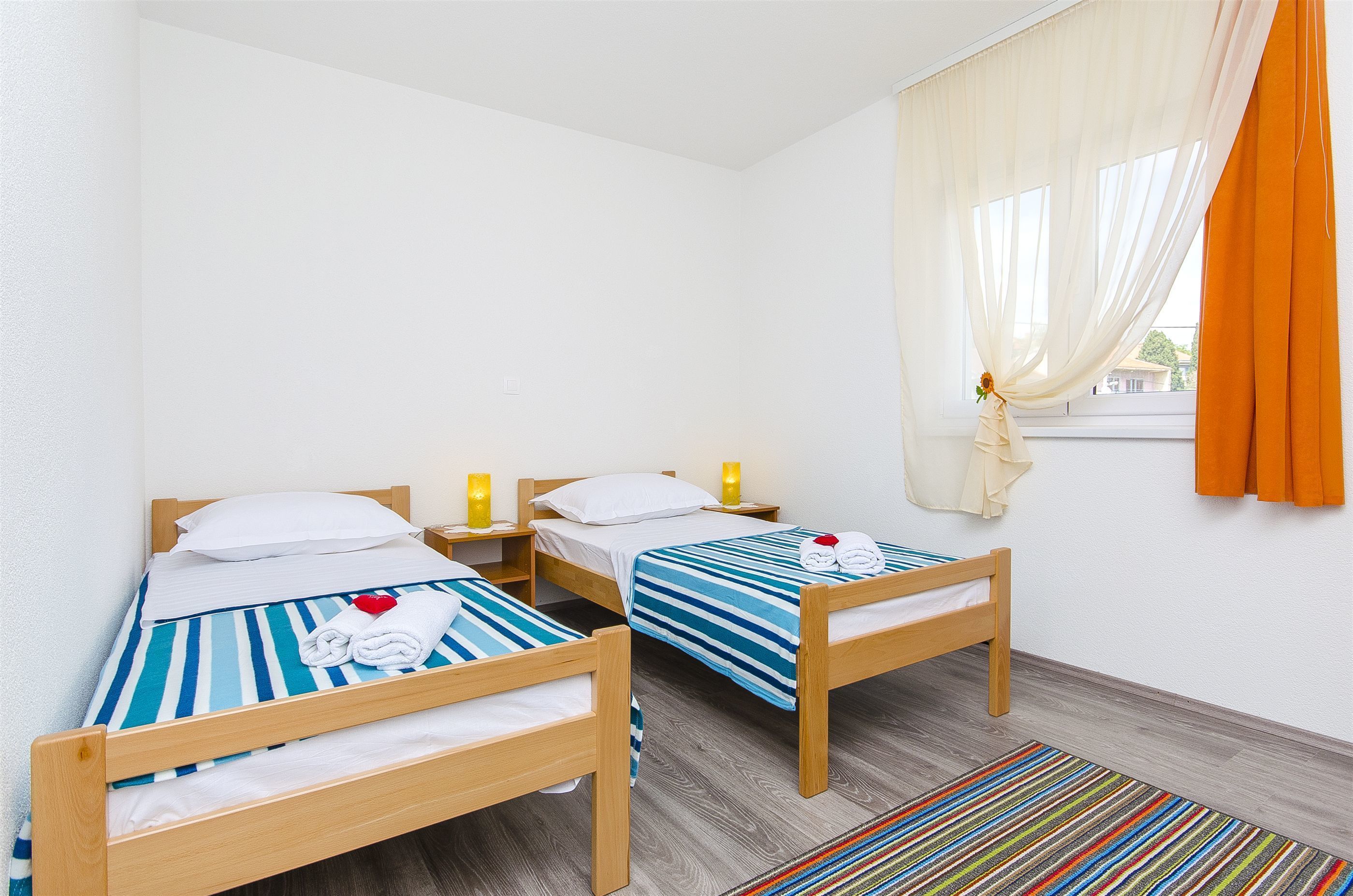 A room with two wooden beds, white bedding, striped blue and white bedsheets, and a colorful striped rug.
