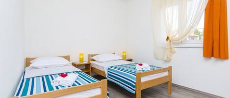 A room with two wooden beds, white bedding, striped blue and white bedsheets, and a colorful striped rug.