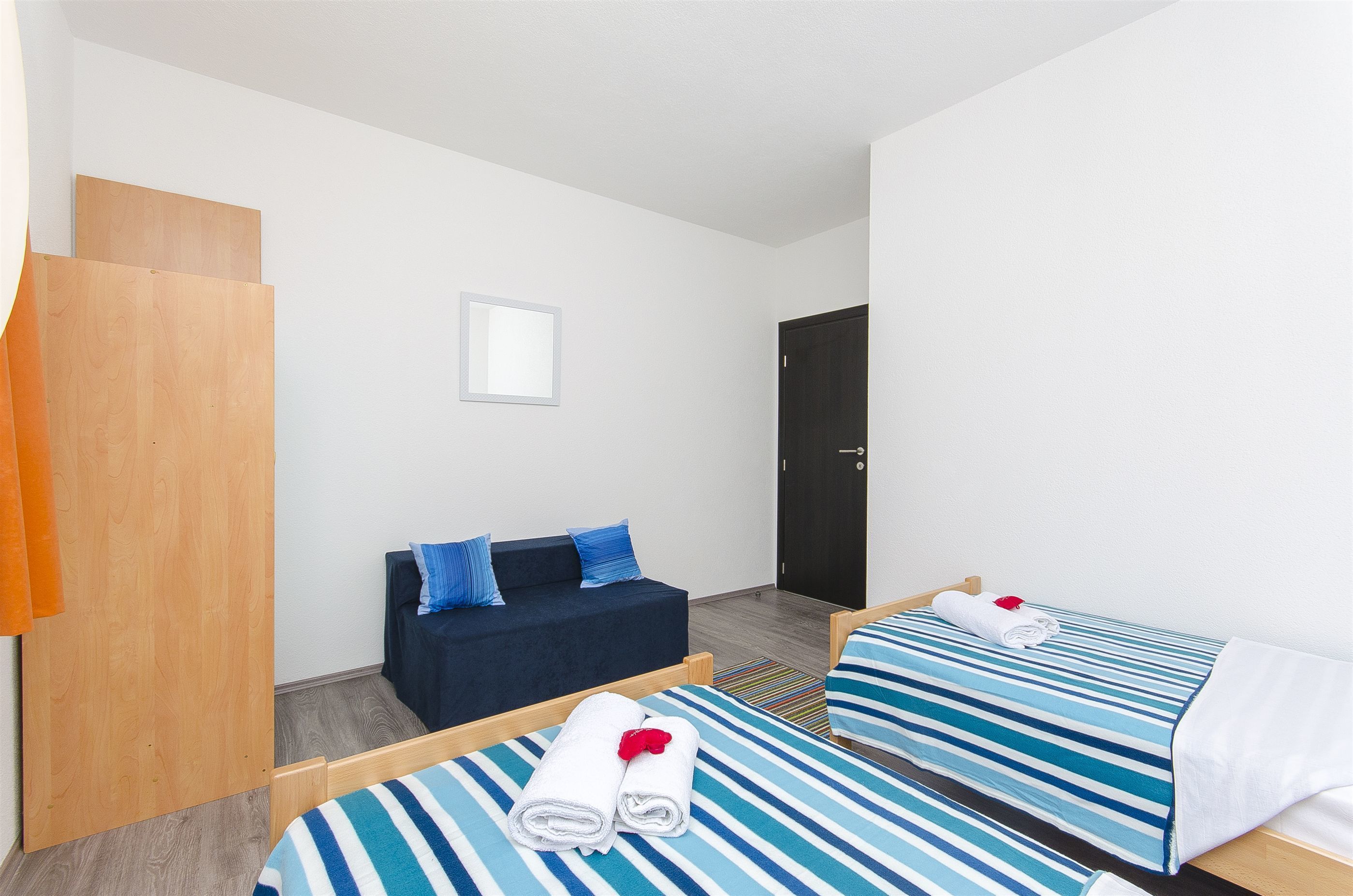 Een hotelkamer met twee bedden, een slaapbank, een houten garderobe en een deur.