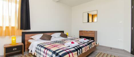 Un dormitorio con cama, mesitas de noche, un espejo y una ventana con cortinas.