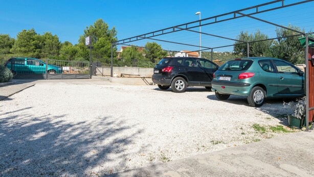 Un estacionamiento con dos autos, superficie de grava y cerca de metal.
