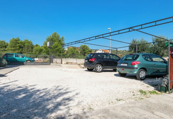 A parking area with two cars, a gravel surface, and a metal fence.