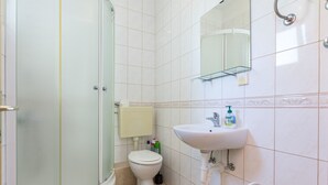 Un baño con ducha separada por mampara de vidrio, inodoro, lavamanos y espejo.
