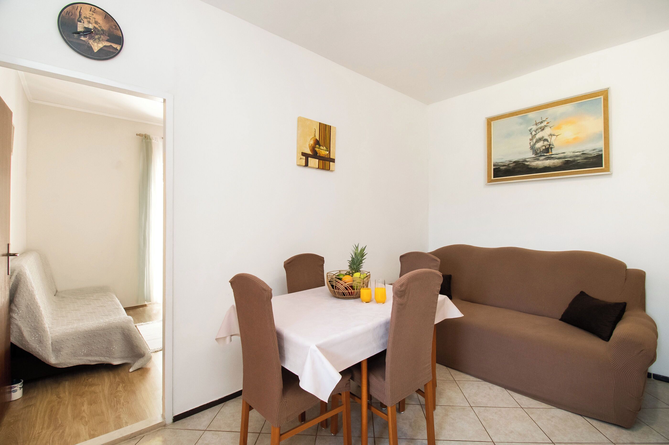Un coin repas avec une table, des chaises et un canapé marron. Il y a une horloge au mur et un tableau au-dessus du canapé.