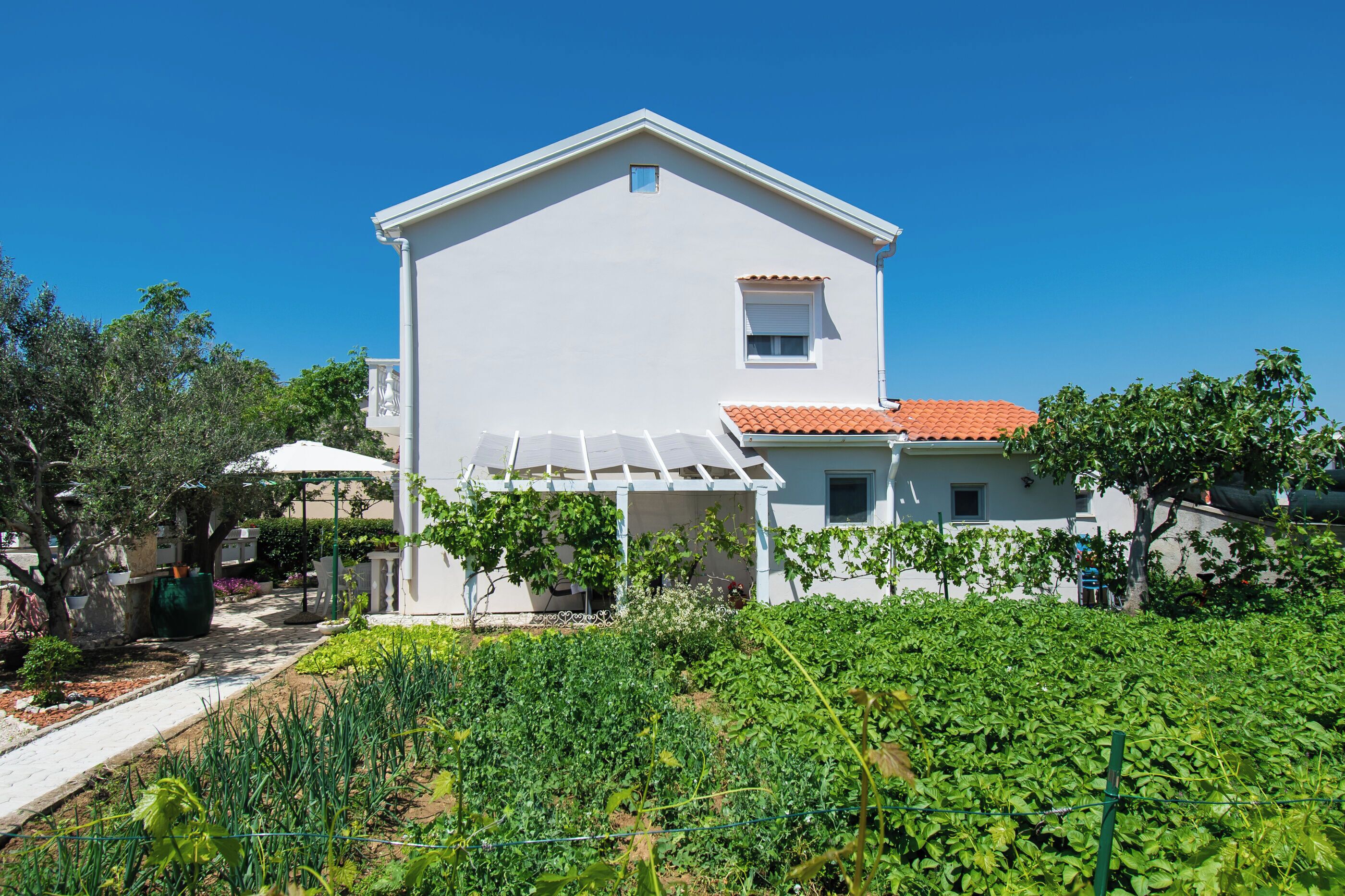 A white building with a red-tiled roof, a small window, and a covered patio area.