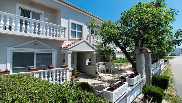 A two-story house with a balcony, potted plants, and a well-maintained garden. - Apartment Ivan Vrsi (Vrsi)
